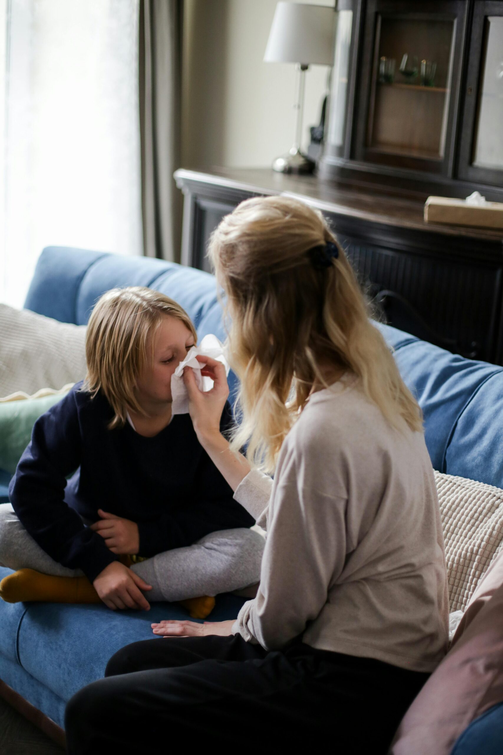 A mother tends to her sick child with a tissue on the couch, showcasing care and comfort.